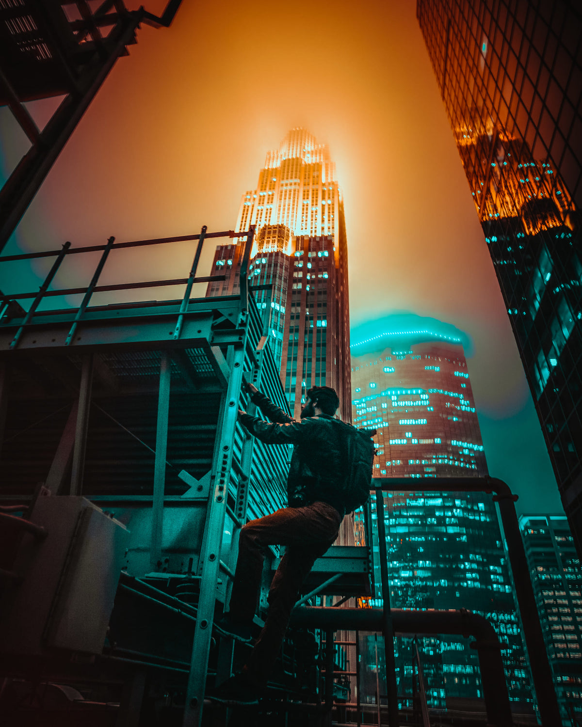 A man climbing up a ladder in front of a backdrop of sky scrapers at night edited to a vibrant teal and orange look