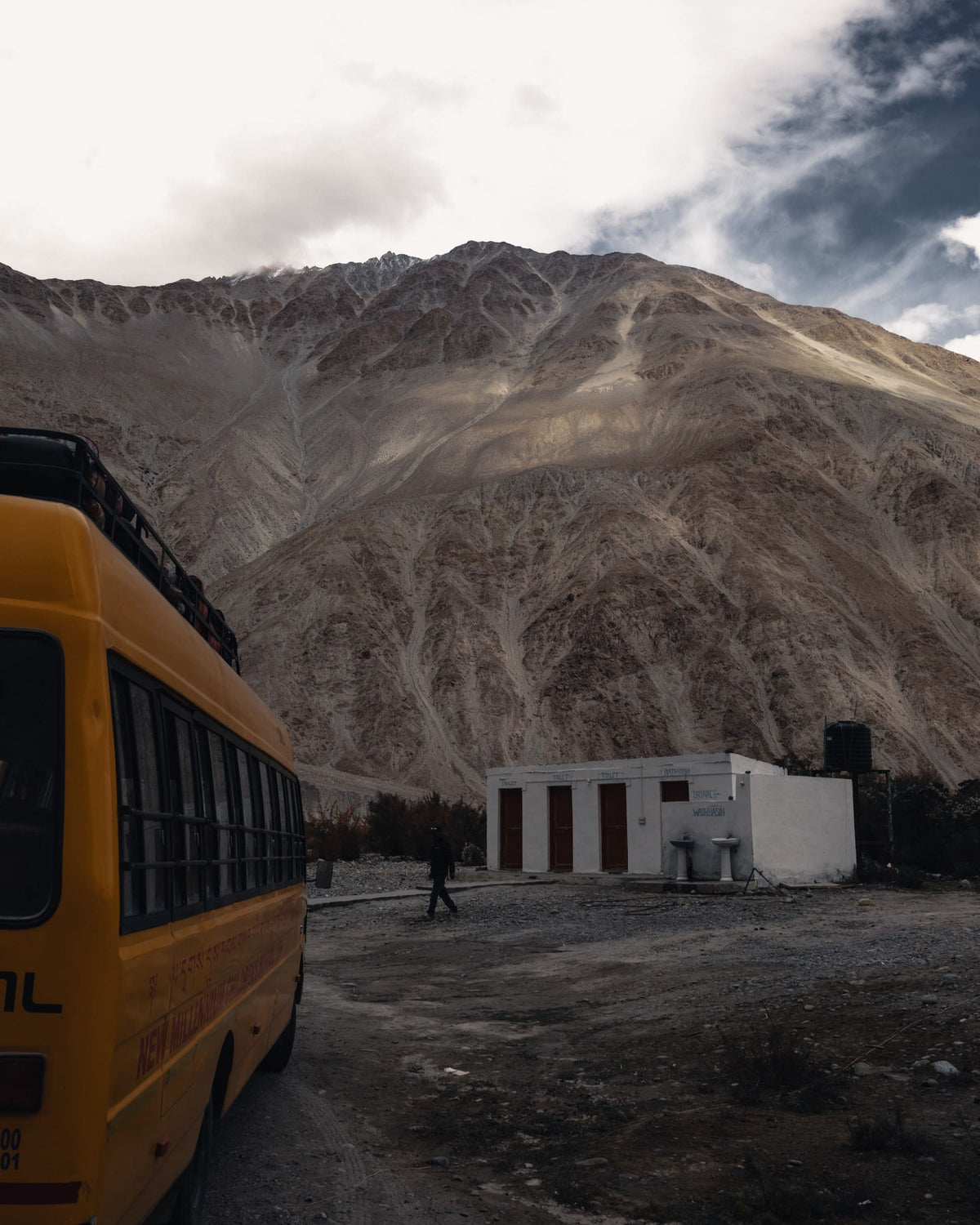 Yellow bus beneath a rugged mountain range, edited with a desaturated Lightroom preset for muted earth tones