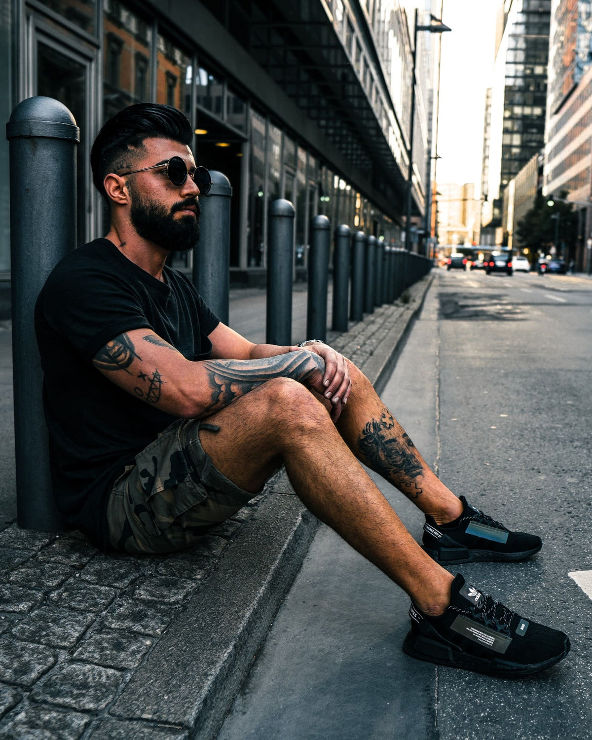 Street portrait of a man in sunglasses seated on a city pavement, edited with Dark Tones Lightroom presets