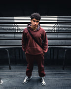 Street portrait of a man in a burgundy tracksuit at the top of a flight of stairs, with deep shadows and subdued colours