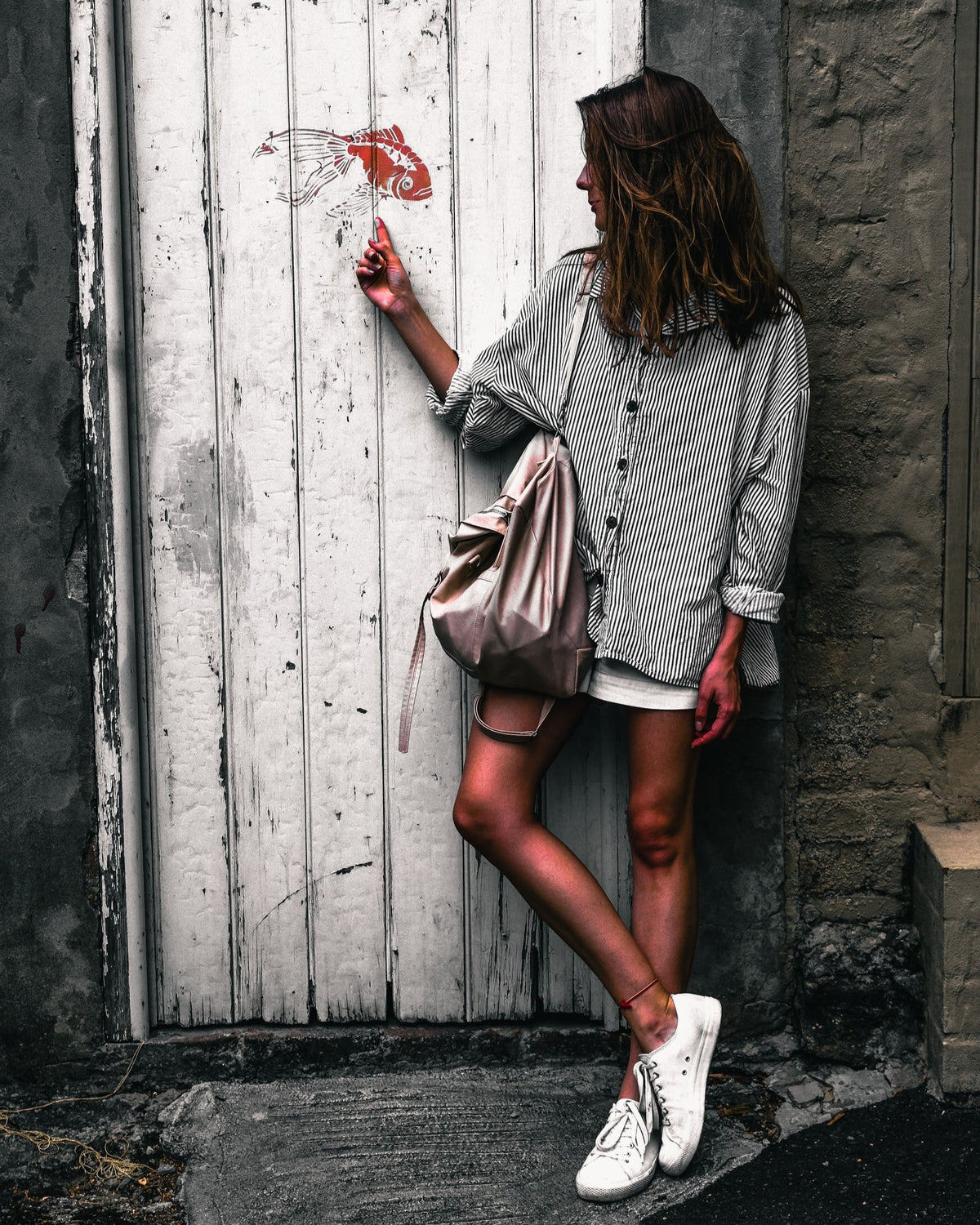 Woman in a striped shirt beside a weathered white door, edited with Dark Tones Lightroom presets for muted colours