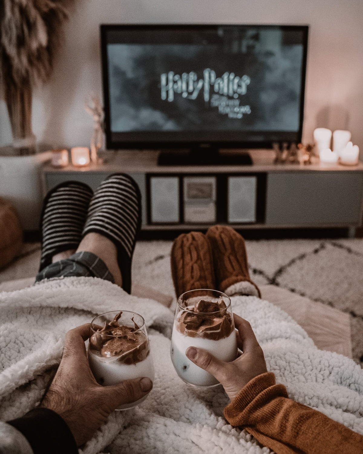 Two people holding whipped coffee drinks during a cosy movie night, edited with a Moody Brown preset
