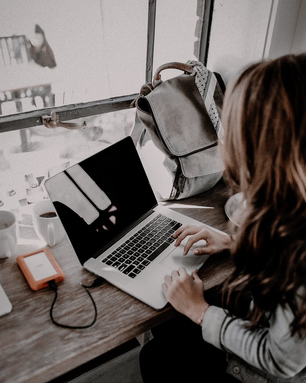 Person using a laptop beside a window, with muted colours and earthy brown tones
