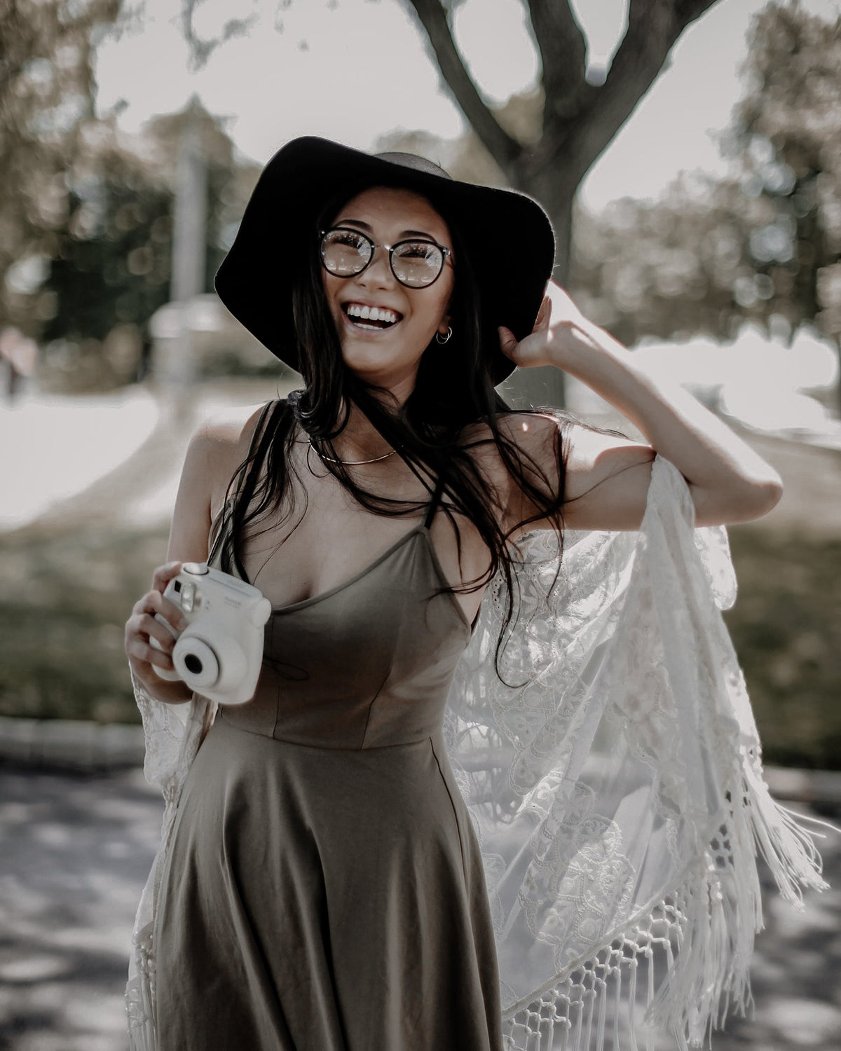 Outdoor portrait of a woman holding an instant camera, with muted greens and earthy brown tones